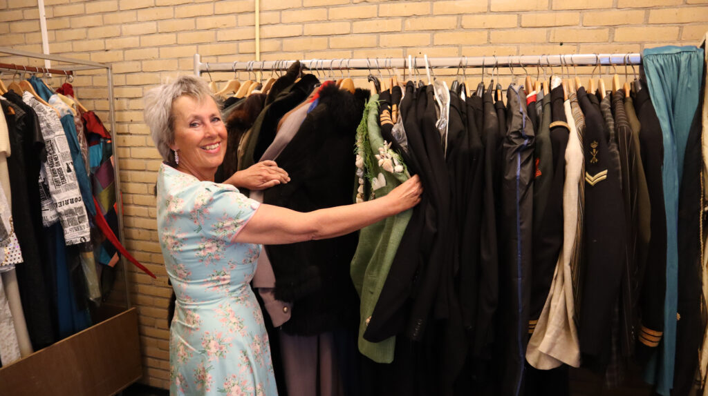 Anne-Gre van Theatergroep Maarssen32 in het nieuwe pand, toont de kostuums.
